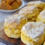 Peri peri pumpkin scones stacked on a wooden board, one split open showing the soft orange crumb