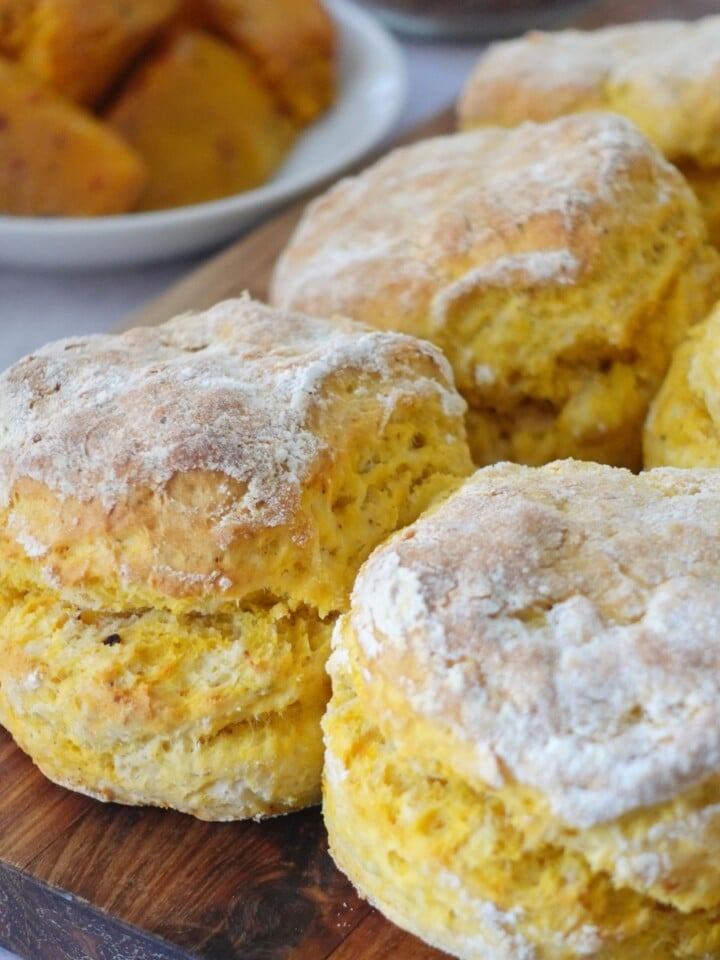 Peri peri pumpkin scones stacked on a wooden board, one split open showing the soft orange crumb