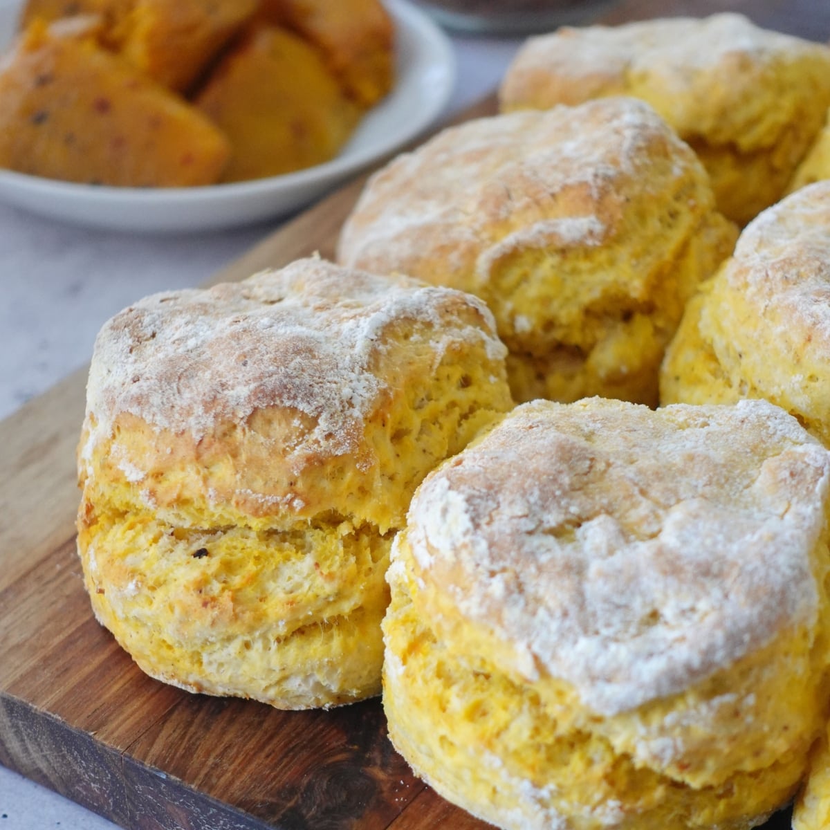 Peri peri pumpkin scones stacked on a wooden board, one split open showing the soft orange crumb