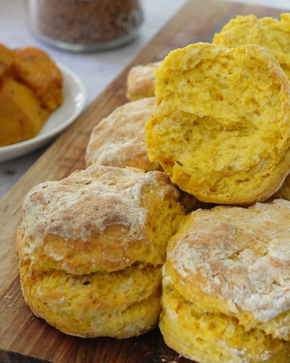 Peri peri pumpkin scones stacked on a wooden board with one split open showing the soft spiced crumb
