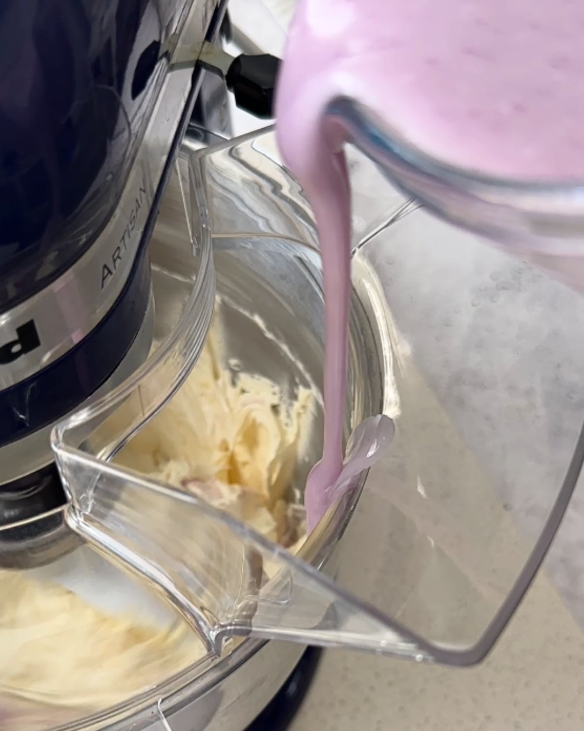 Pouring ube sugar mixture into whipped butter in a stand mixer