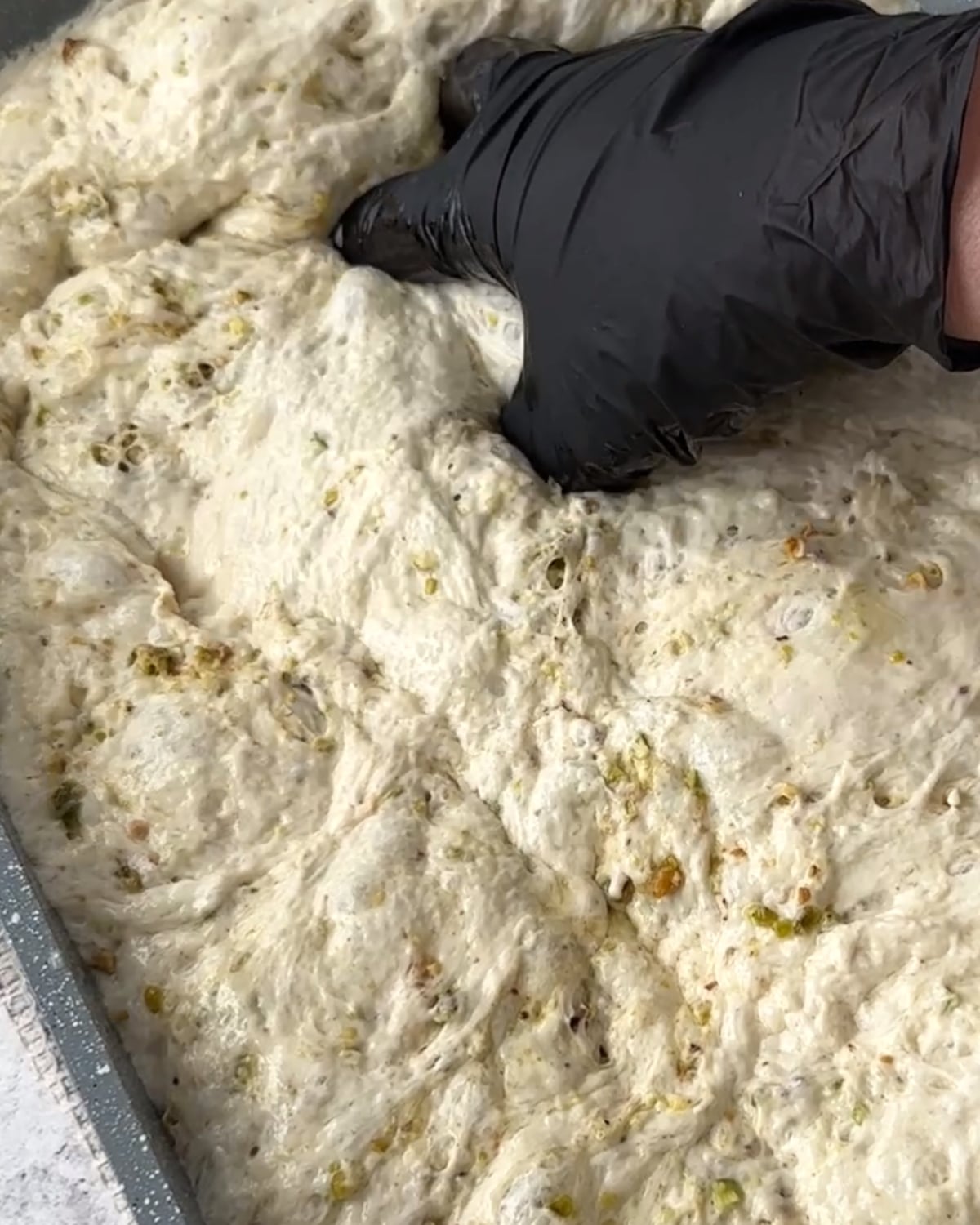 Spoon scattering crushed pistachios over baked focaccia drizzled with pistachio cream
