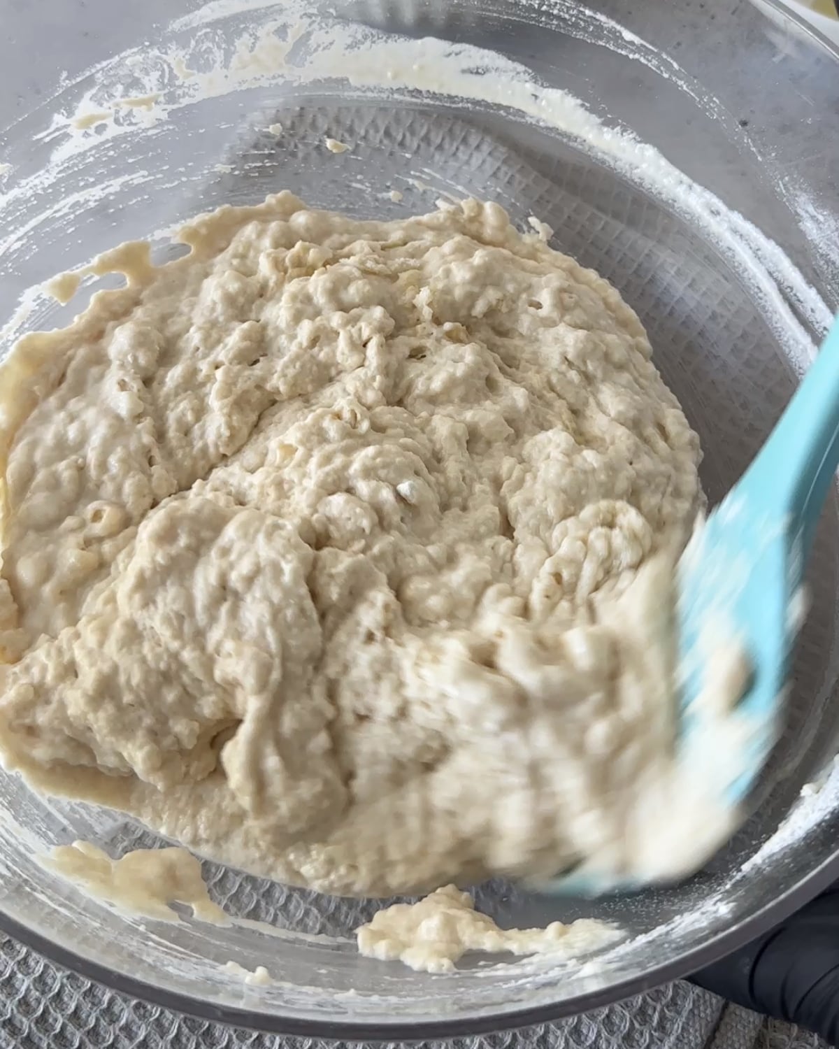 Wet, sticky focaccia dough just mixed in a glass bowl with a spatula
