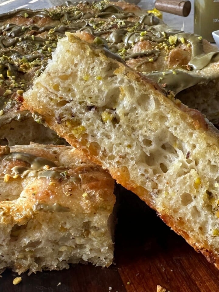 Slice of pistachio focaccia resting on the rest of the bake, topped with drizzled pistachio cream and crushed pistachios