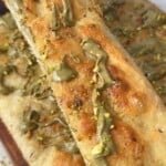 Slice of pistachio focaccia resting on the rest of the bake, topped with drizzled pistachio cream and crushed pistachios