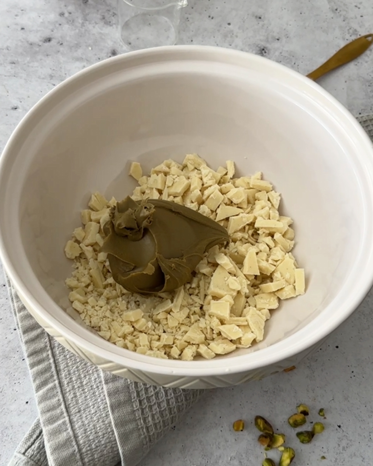 Chopped white chocolate with a scoop of pistachio cream in a white mixing bowl