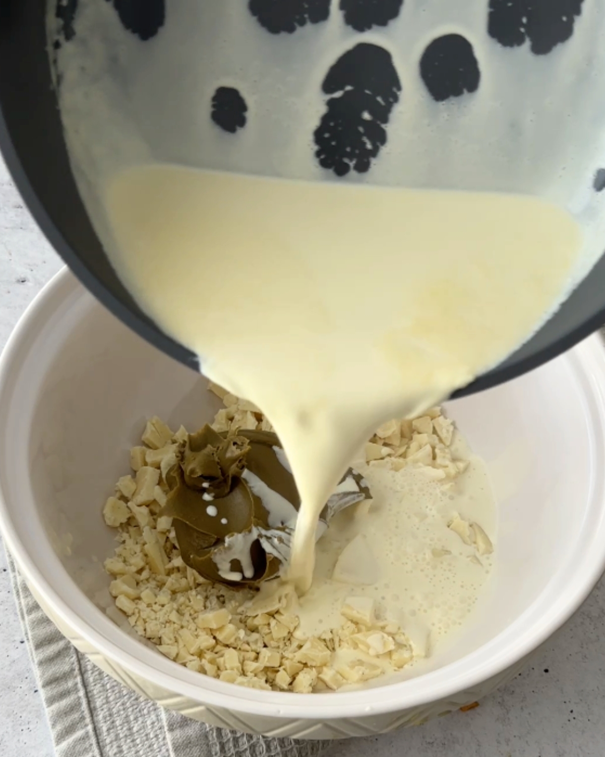 Hot cream poured from a saucepan over chopped white chocolate and pistachio cream