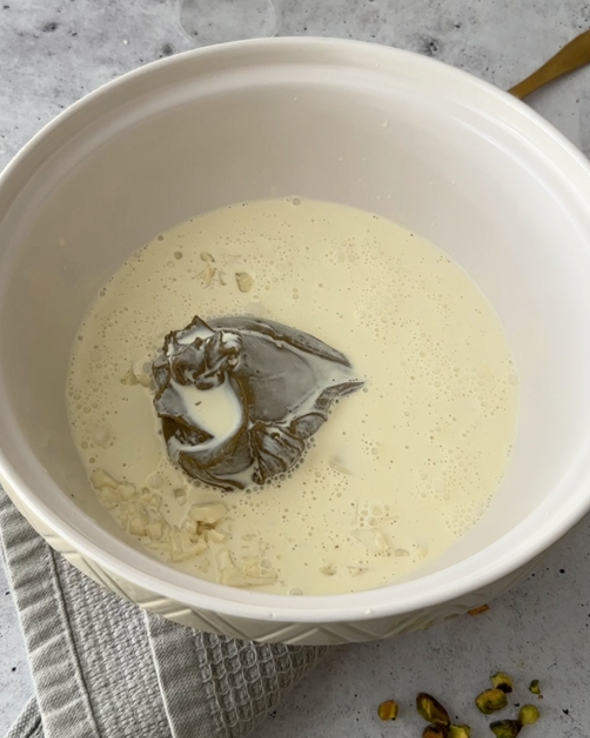 Hot cream covering chopped white chocolate and pistachio cream in a mixing bowl