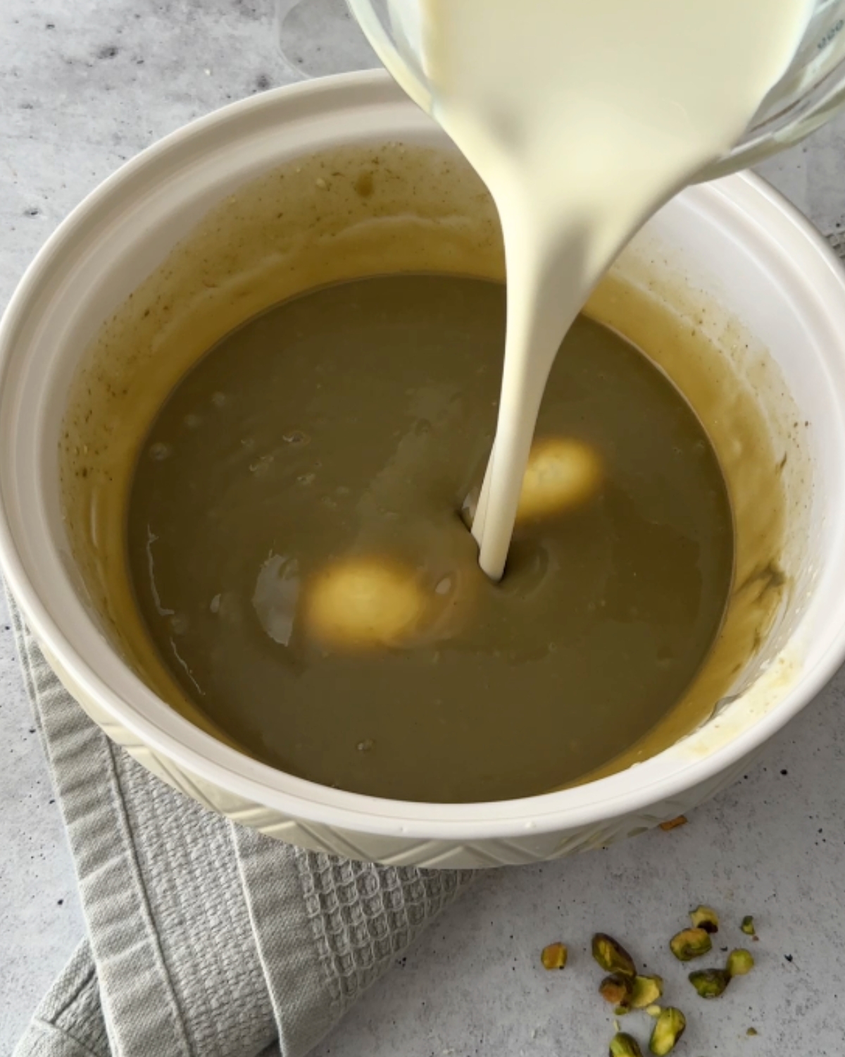 Cold cream poured from a glass jug into smooth pistachio white chocolate ganache