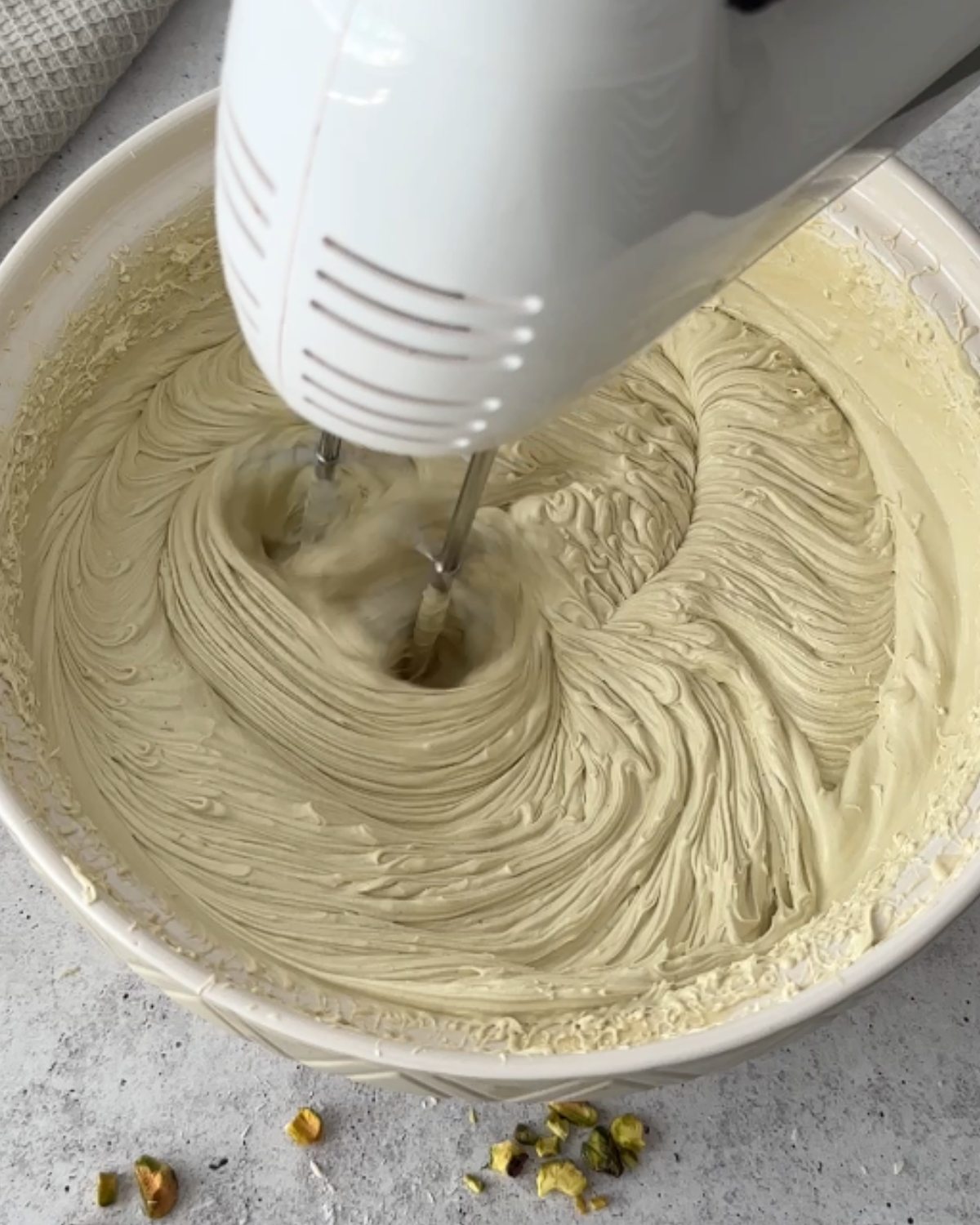Hand mixer whipping chilled ganache in a white bowl, with trails forming in the mixture