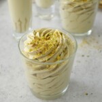Pistachio mousse with white chocolate piped into small glasses and topped with chopped pistachios