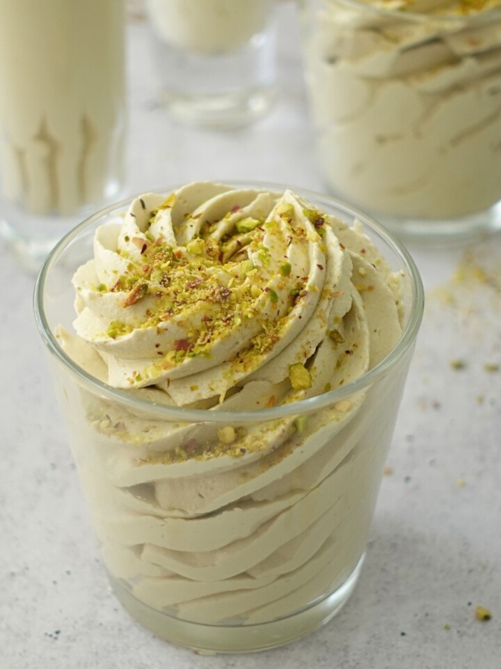Pistachio mousse with white chocolate piped into small glasses and topped with chopped pistachios