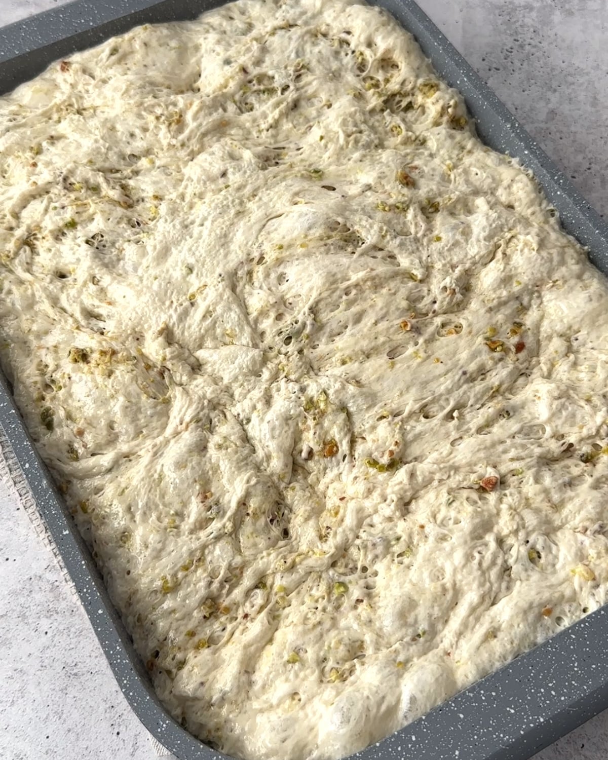 Puffy risen focaccia dough with pistachio pieces filling a baking pan